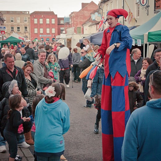 Stilt-walking jester at festival web sqr